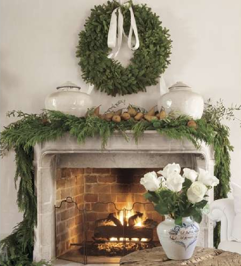 Breathtaking with natural greenery, antique French pots, and pears, a stone fireplace is decorated for the holidays in Pamela Pierce's Houston home. #christmasfireplace #christmasmantel #frenchcountry #whitechristmas #christmasdecor #pamelapierce #milieumag