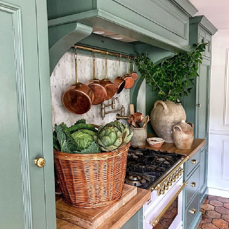 Glorious French farmhouse kitchen with antique decor, Neptune designed kitchen with cabinets painted Farrow & Ball Green Smoke, and charming reclaimed antique terra cotta hex floor tiles - Vivi et Margot. #frenchfarmhouse #frenchkitchen #rustickitchens #farrowandballgreensmoke #antiquedecor #copperpots #ilverange