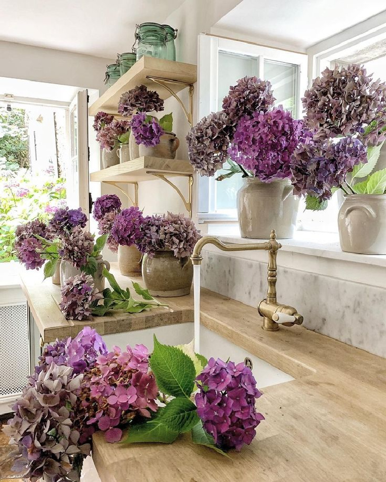 Lovely end of summer purple hydrangeas in a beautiful French farmhouse kitchen with wood countertops - Vivi et Margot. #frenchfarmhouse #frenchcountry #hydrangea #frenchkitchen #countrykitchens #woodcountertop #kitcheninfrance
