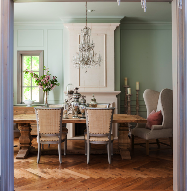 French Country design in a dining room with pedestal farm table, herringbone wood flooring, limestone fireplace, and blue grey trim. Design by Decor de Provence. #FrenchCountry #diningroom #FrenchNordic