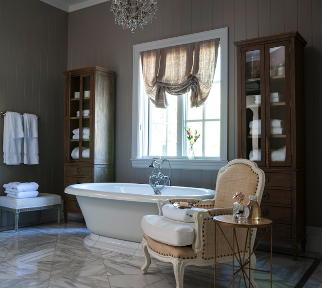 French Country cottage bathroom decor with freestanding tub, French chair, and glass fronted cabinets storing towels. Decor de Provence.