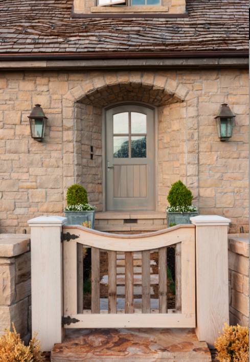 Limestone facade of French Country cottage with beautiful arched wood door, garden gate, and slate roof. #frenchcountry #cottagestyle #stonecottage