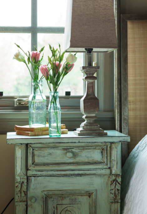 Green stained side table with green bottles and rustic wood lamp in a French country cottage by Decor de Provence in Utah. Come be inspired by interior design photos with French Green Paint Colors and Serene French Blue-Greens. #greenpaintcolors #mintgreen #interiordesign #paint