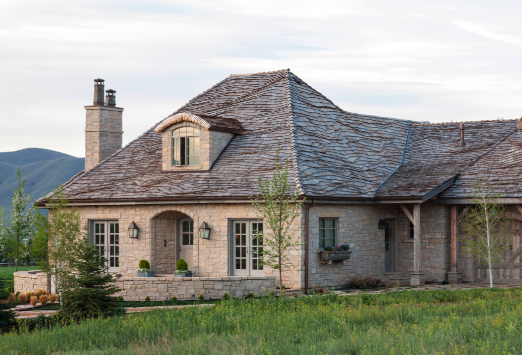 French Country style home exterior with stone, slate roof, eyebrow architecture, and Gustavian details. #frenchcountry #frenchcottage #frenchfarmhouse #exterior