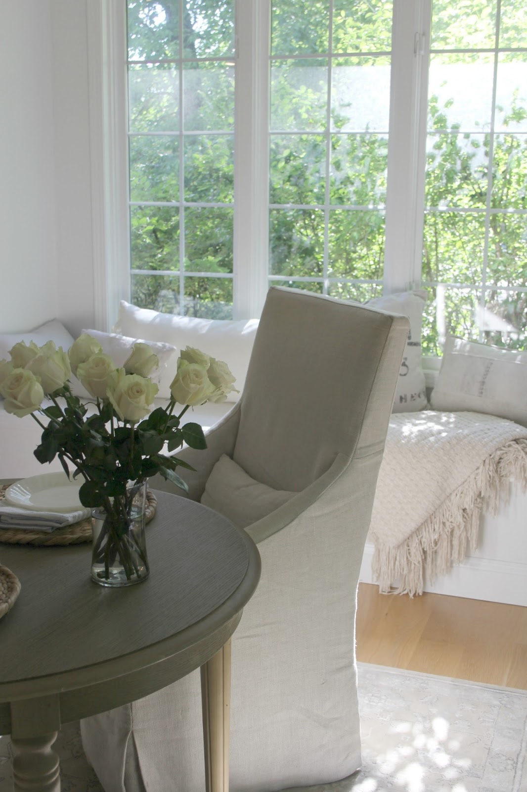 Window seat in white kitchen with dappled natural light, white roses, and European inspired decor. #hellolovelystudio #belgianlinen #windowseat