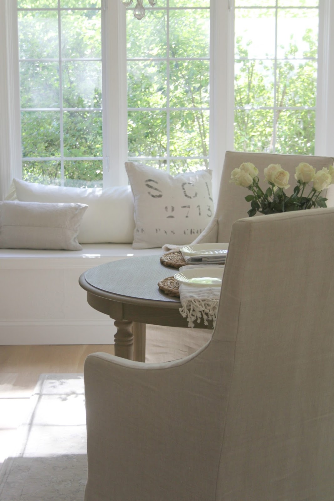 Serene white kitchen decor with window seat and linen pillows in a soft, timelessly romantic kitchen by Hello Lovely Studio. #kitchendecor #whitekitchen #frenchcountry #windowseat #belgianilnen #slipcovers #serene