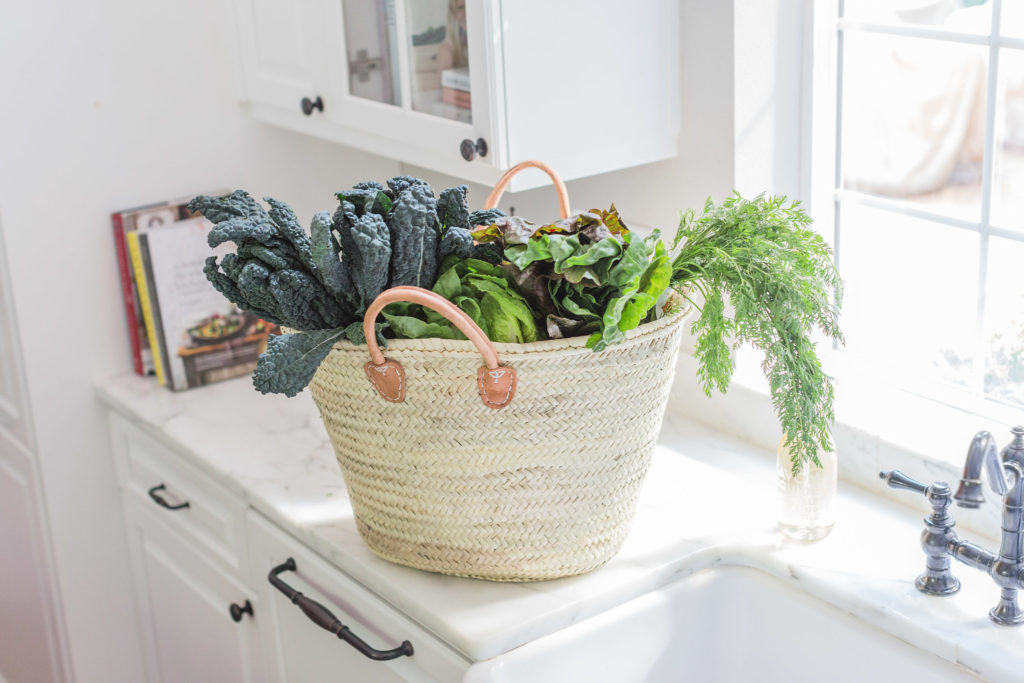 Gorgeous woven market tote with farm fresh greens and vegetables in white kitchen with marble. Lemon Grove Lane.