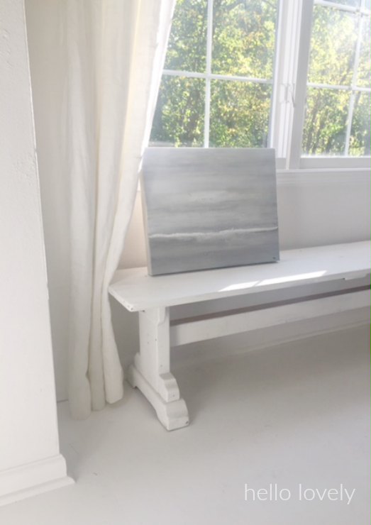 An abstract seascape by me rests on a reclaimed barn wood bench. White flooring and white linen curtains (RH). #hellolovelystudio #whitedecor #whitepaintedfloor #farmbench #abstractpainting #seascape #whitelinencurtains