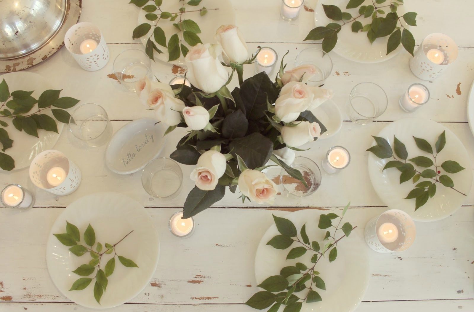 Romantic white tablescape with blush roses, green branches, and candlelight by Hello Lovely Studio
