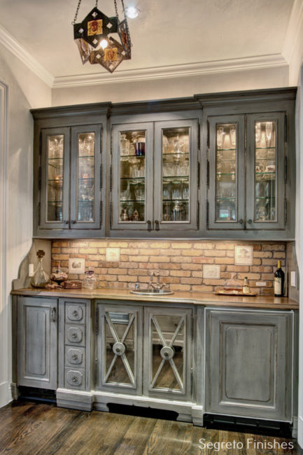 Gorgeous paint finish by Segreto to grey cabinets in a bar area with brick backsplash