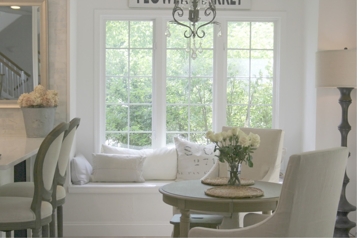 Serene white decor in breakfast nook with window seat and Belgian linen upholstery - Hello Lovely Studio. #kitchendecor #breakfastnook #windowseat #frenchfarmhouse #europeancountry #belgianlinen #frenchcountry #interiordesign