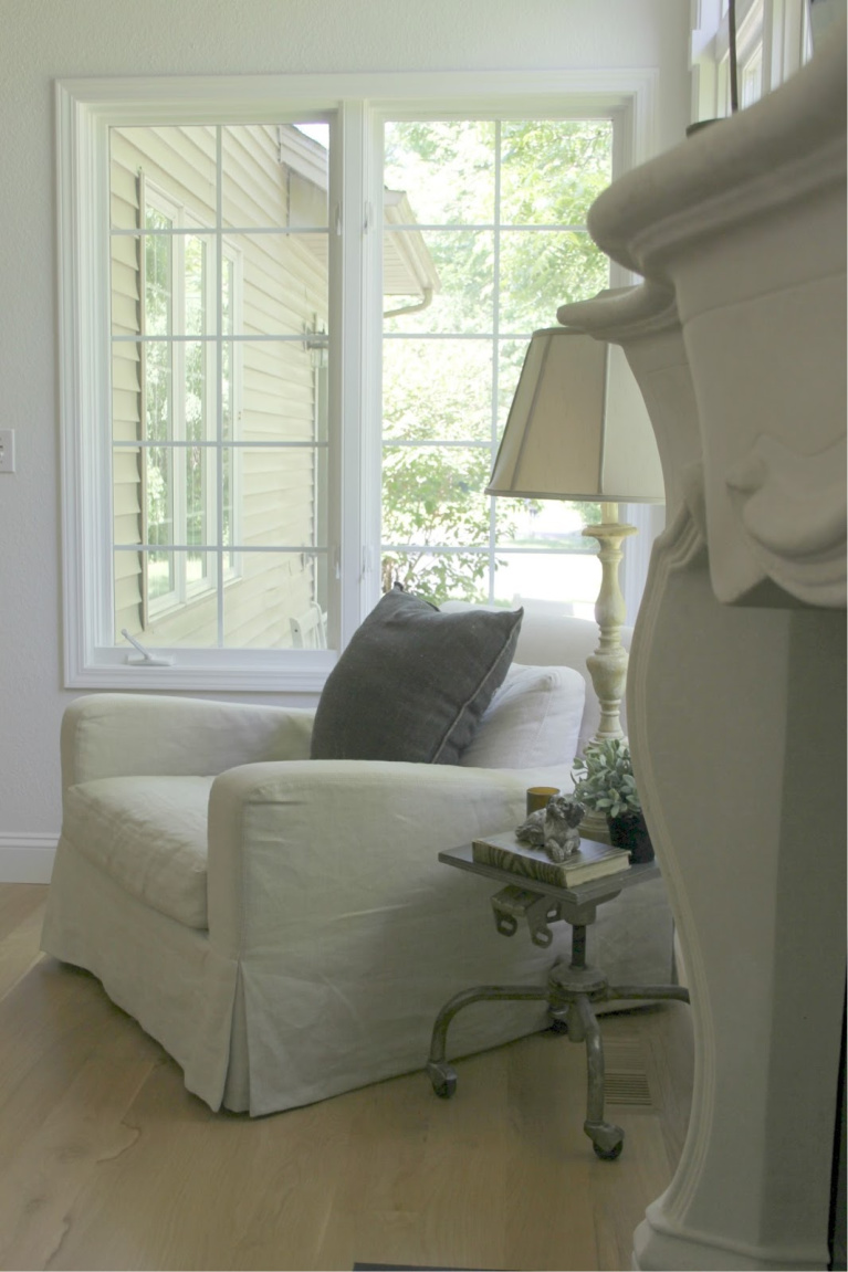 Belgian linen club chair with industrial accent table in my European country living room with French fireplace. #hellolovelystudio #belgianlinen #livingroomdecor #europeancountry #belgianstyle #serenedecor #interiordesign