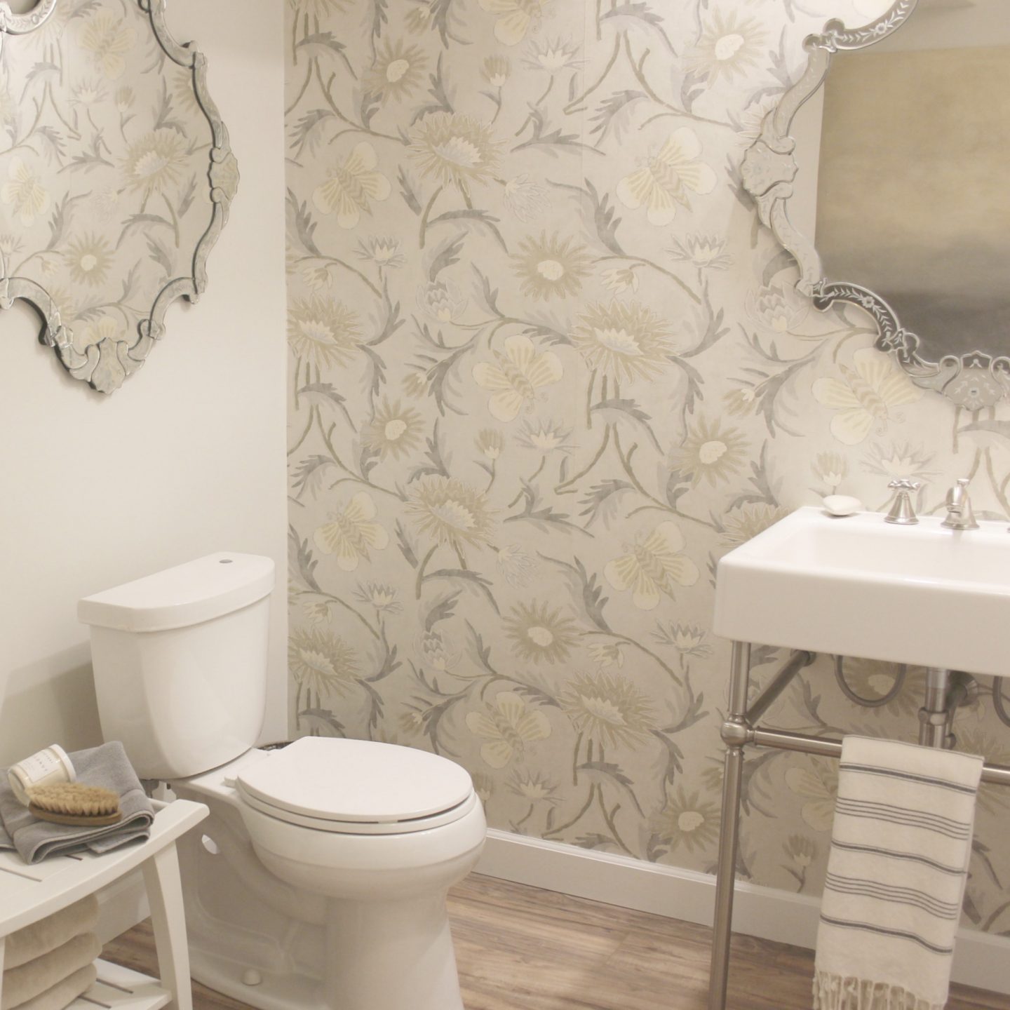 Venetian mirrors, a console sink, wallpaper, and classic decor details in a bathroom created in an ugly, dark basement. #beforeandafter #bathroomdesign #DIYbathroom #consolesink