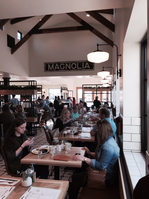 Magnolia Table restaurant interior with ceiling beams, Magnolia sign, subway tile, and black and white decor. #magnoliatable #farmhousestyle #restaurant #fixerupper