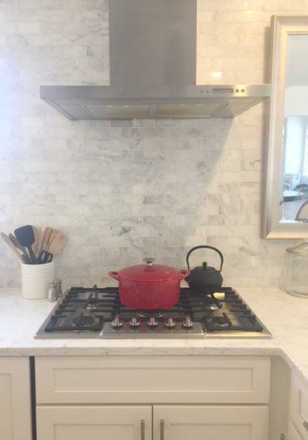 Red cast iron dutch oven on cooktop with marble subway tile backsplash. #red #dutchoven #marblebacksplash