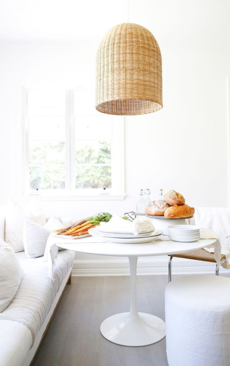 All white modern rustic decor in a chic breakfast nook in the kitchen with Saarinen table, sofa, and wicker pendant light. Erin Fetherston's white California farmhouse is chic yet livable with a Midcentury Modern twist. #allwhite #saarinen #whitekitchen #midcentury #breakfastnook