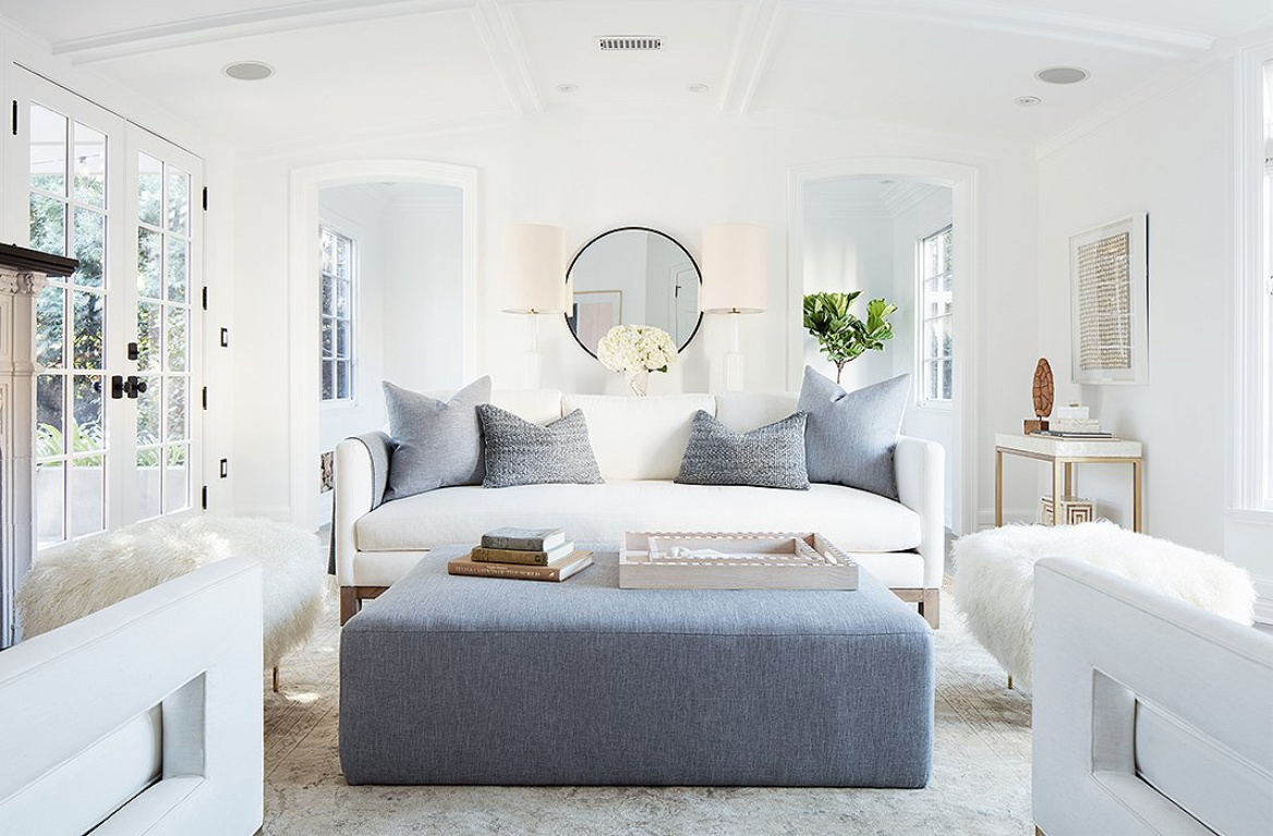 Midcentury modern style in a modern farmhouse living room with white decor. “I wanted every wall to make sense, to have its own vignette,” says Alex. It’s also a flexible design scheme—the ottoman adds extra seating and can be “scooched up for cozier conversations during parties.” #blueandwhite #livingroom #modernrustic #serenedecor #interiordesign