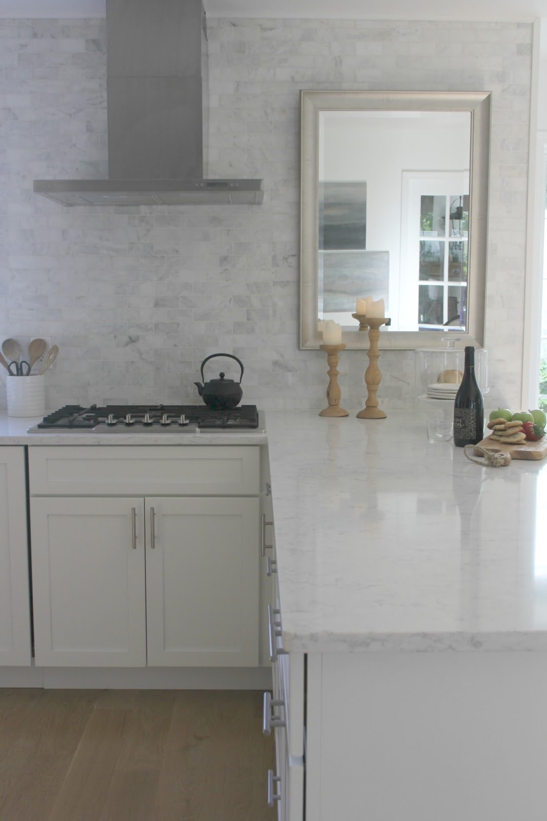 White kitchen with modern European farmhouse style, white quartz counter, Italian range hood, marble subway tile, and cooktop. Design by Hello Lovely Studio. #whitekitchen #modernfarmhouse #classic #european #timeless #serene #hellolovelystudio