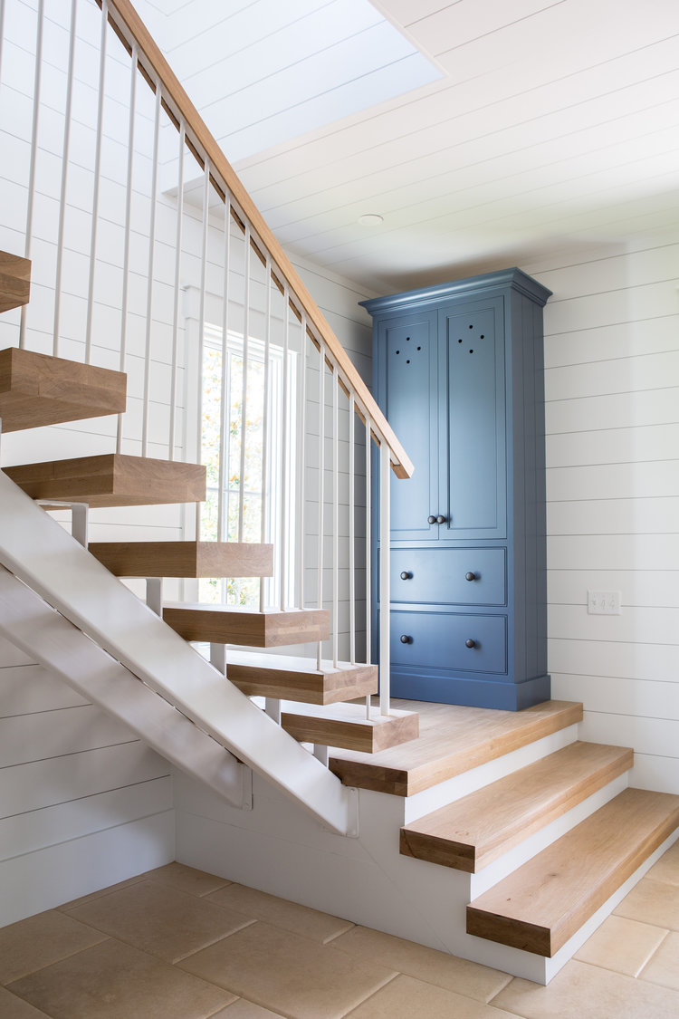 White oak staircase, shiplap, and blue armoire in entry. Board and batten coastal cottage in Palmetto Bluff with modern farmhouse interior design by Lisa Furey.