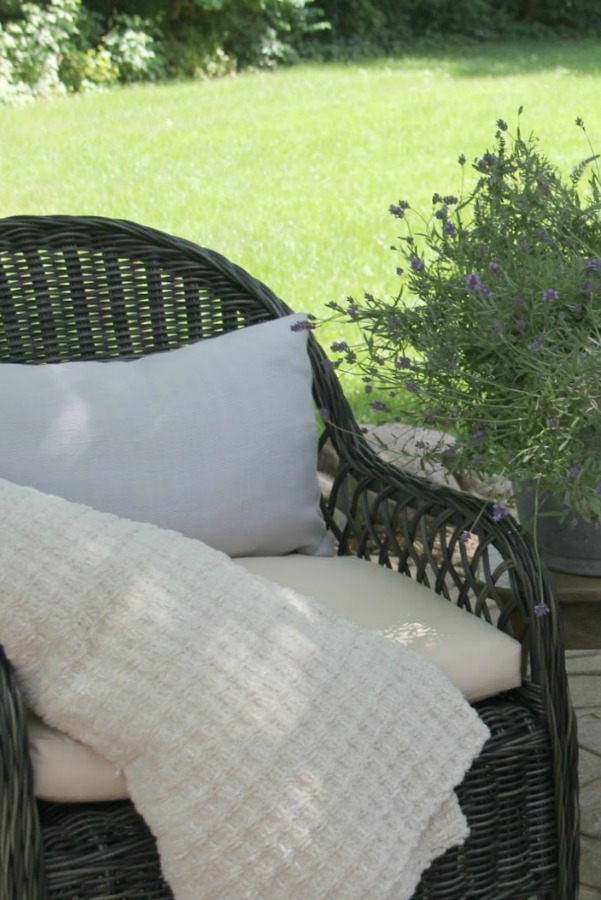 A light grey linen pillow (RH) and an ivory chenille throw (RH) soften a grey rattan patio chair on my backyard patio - Hello Lovely Studio.