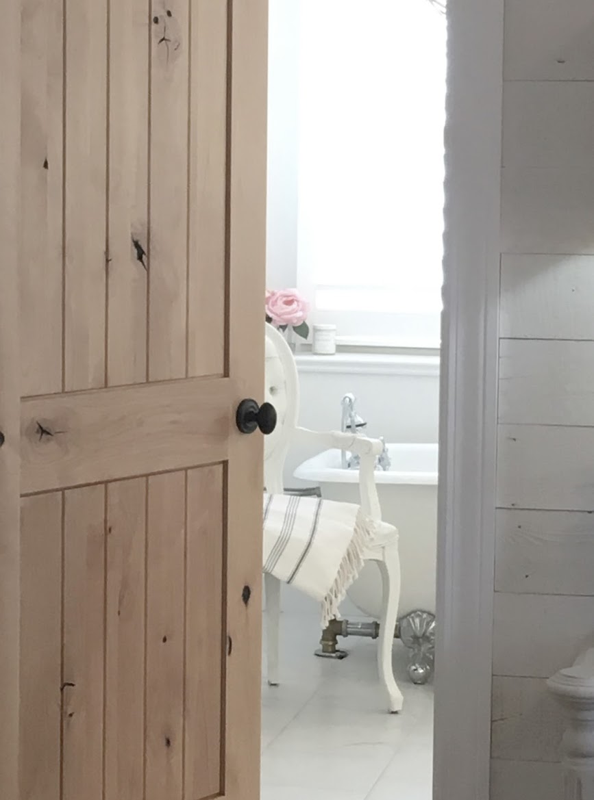 Knotty alder door ajar in serene white bathroom by Hello Lovely Studio. #hellolovelystudio #alder #vintagedoor
