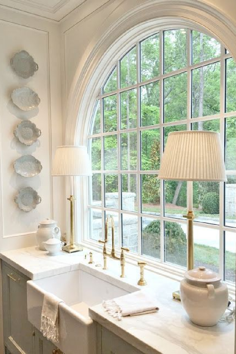 French Country interior design inspiration from a classic kitchen with blue and white decor! Stunning traditional style kitchen with light blue painted cabinets, hammered brass hardware arch window over farm sink, and waterfall marble island.