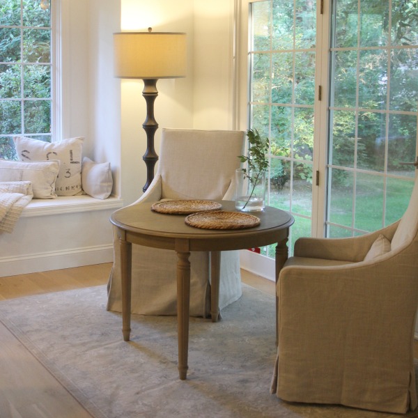 Serene European inspired kitchen with Belgian linen upholstered arm chairs, round dining table, and window seat. Hello Lovely Studio. #hellolovelystudio #windowseat #kitchendesign #breakfastroom