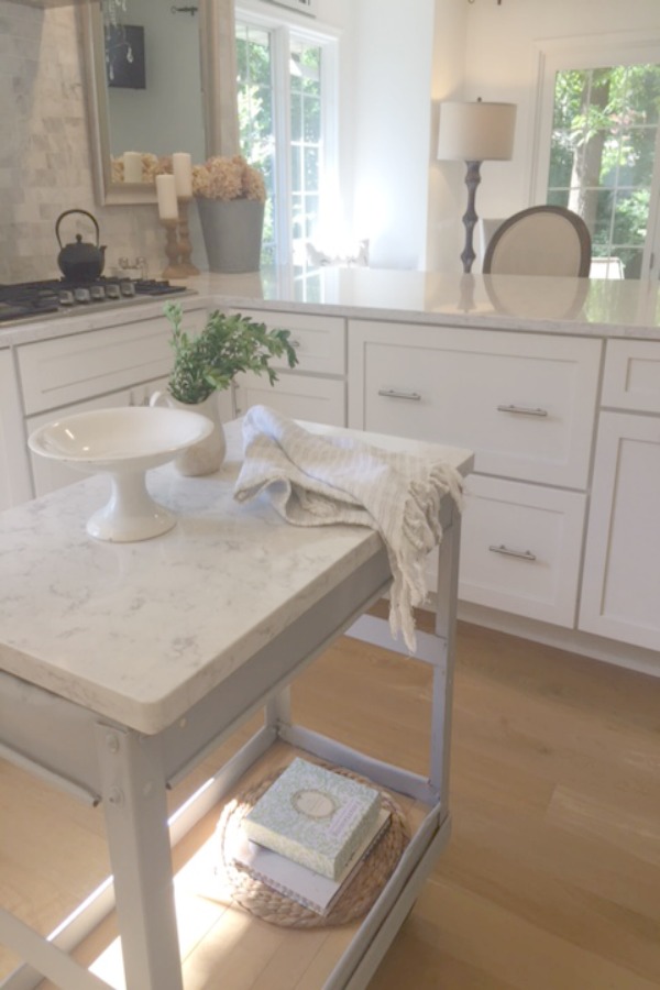 In our Lovely Tranquil Classic Kitchen is a mix of modern and vintage design elements. An industrial steel cart (painted Annie Sloan Paris Grey), Shaker cabinetry, marble subway tile backsplash, stainless pro appliances, fireclay farm sink, white oak hardwood flooring, and Viatera Minuet quartz on counters. #hellolovelystudio #whitekitchen #serenedecor #timelessdesign #modernfarmhouse #europeanfarmhouse #industrialcart #marblesubwaytile #whiteoak #viateraquartz #minuet #anniesloanparisgrey #steelcart