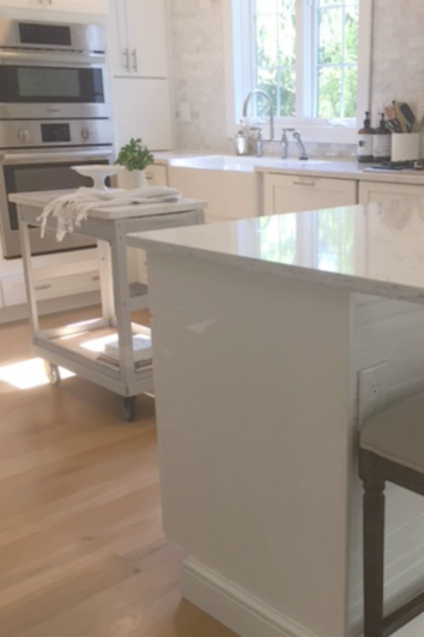 In our Lovely Tranquil Classic Kitchen is a mix of modern and vintage design elements. An industrial steel cart (painted Annie Sloan Paris Grey), Shaker cabinetry, marble subway tile backsplash, stainless pro appliances, fireclay farm sink, white oak hardwood flooring, and Viatera Minuet quartz on counters. #hellolovelystudio #whitekitchen #serenedecor #timelessdesign #modernfarmhouse #europeanfarmhouse #industrialcart #marblesubwaytile #whiteoak #viateraquartz #minuet #anniesloanparisgrey #steelcart