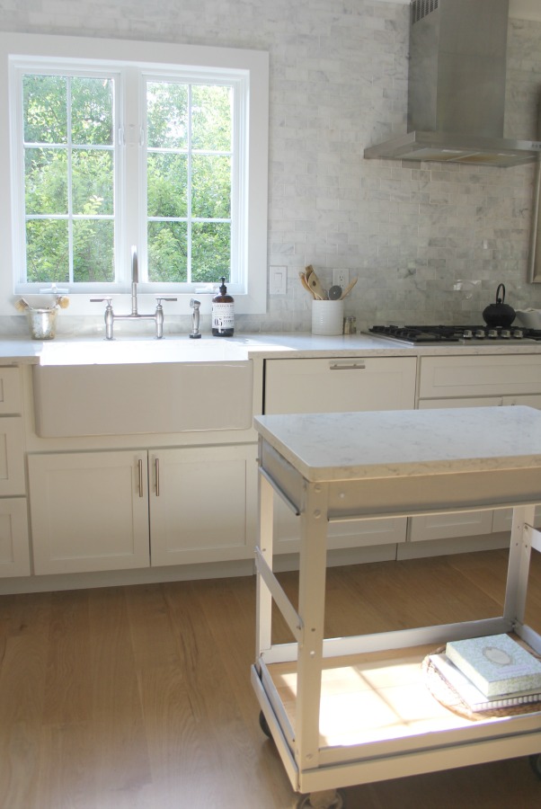 In our Lovely Tranquil Classic Kitchen is a mix of modern and vintage design elements. An industrial steel cart (painted Annie Sloan Paris Grey), Shaker cabinetry, marble subway tile backsplash, stainless pro appliances, fireclay farm sink, white oak hardwood flooring, and Viatera Minuet quartz on counters. #hellolovelystudio #whitekitchen #serenedecor #benjaminmoorewhite #timelessdesign #modernfarmhouse #europeanfarmhouse #industrialcart #marblesubwaytile #whiteoak #viateraquartz #minuet #anniesloanparisgrey #steelcart