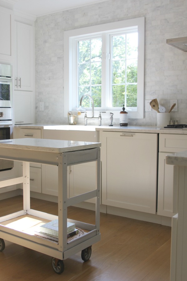 In our Lovely Tranquil Classic Kitchen is a mix of modern and vintage design elements. An industrial steel cart (painted Annie Sloan Paris Grey), Shaker cabinetry, marble subway tile backsplash, stainless pro appliances, fireclay farm sink, white oak hardwood flooring, and Viatera Minuet quartz on counters. #hellolovelystudio #whitekitchen #serenedecor #timelessdesign #modernfarmhouse #europeanfarmhouse #industrialcart #marblesubwaytile #whiteoak #viateraquartz #minuet #anniesloanparisgrey #steelcart