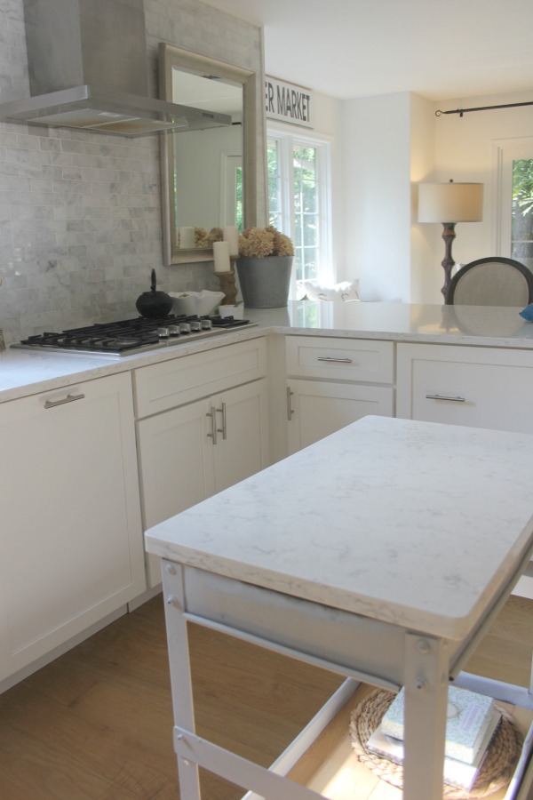 In our Lovely Tranquil Classic Kitchen is a mix of modern and vintage design elements. An industrial steel cart (painted Annie Sloan Paris Grey), Shaker cabinetry, marble subway tile backsplash, stainless pro appliances, fireclay farm sink, white oak hardwood flooring, and Viatera Minuet quartz on counters. #hellolovelystudio #whitekitchen #serenedecor #timelessdesign #modernfarmhouse #europeanfarmhouse #industrialcart #marblesubwaytile #whiteoak #viateraquartz #minuet #anniesloanparisgrey #steelcart