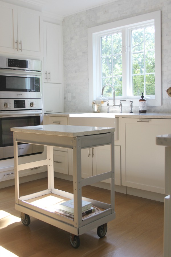 In our Lovely Tranquil Classic Kitchen is a mix of modern and vintage design elements. An industrial steel cart (painted Annie Sloan Paris Grey), Shaker cabinetry, marble subway tile backsplash, stainless pro appliances, fireclay farm sink, white oak hardwood flooring, and Viatera Minuet quartz on counters. #hellolovelystudio #whitekitchen #serenedecor #timelessdesign #modernfarmhouse #europeanfarmhouse #industrialcart #marblesubwaytile #whiteoak #viateraquartz #minuet #anniesloanparisgrey #steelcart