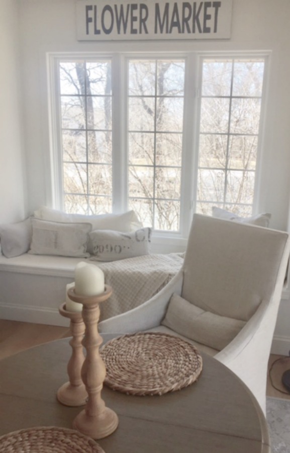 Flower market sign hangs above window seat in serene space. In our Lovely Tranquil Classic Kitchen is a mix of modern and vintage design elements. An industrial steel cart (painted Annie Sloan Paris Grey), Shaker cabinetry, marble subway tile backsplash, stainless pro appliances, fireclay farm sink, white oak hardwood flooring, and Viatera Minuet quartz on counters. #hellolovelystudio #whitekitchen #serenedecor #timelessdesign #modernfarmhouse #europeanfarmhouse #industrialcart #marblesubwaytile #whiteoak #viateraquartz #minuet #anniesloanparisgrey #steelcart