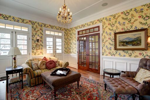 French country living room with yellow floral wallpaper, red oriental rug, and French doors with transom.