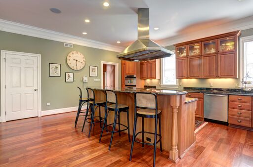 Traditional kitchen design with sage green walls, wood cabinets, hardwood floor and stainless range hood over island cooktop.