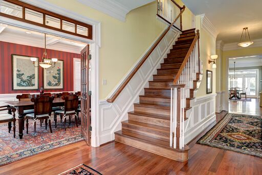 Frenchc ountry entry with wood staircase and red wallpaper on dining room wall.