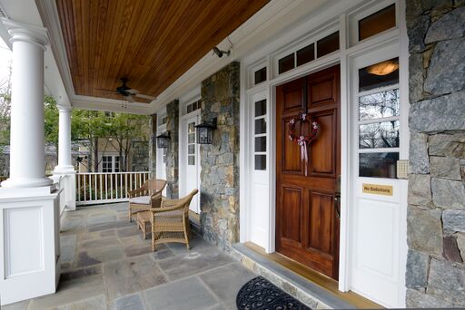 Front porch of stone Colonial house with columns, wood ceiling, and beautiful stone porch floor.