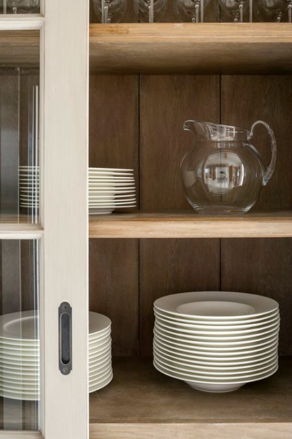 Glass door detail in a bespoke modern rustic country kitchen by Artichoke with large island. This bespoke modern rustic kitchen, designed for a new build country house, takes influence from Flemish design. The large central kitchen island has a specialist finish to age the material and give it a rustic feel. The painted furniture forms a backdrop to the island and has classical detailing with raised and fielded panel doors.Primary materials: Oak, Bental White marble, hand painted furniture and bronze handles #bespoke #kitchendesign #englishcountry #englishkitchen #flemish #modernrustic