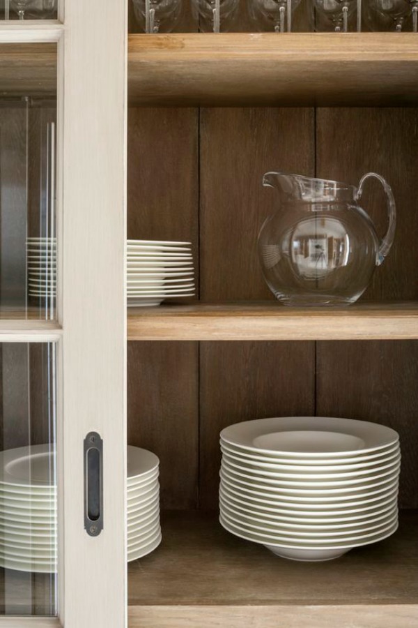 Glass door detail in a bespoke modern rustic country kitchen by Artichoke with large island. This bespoke modern rustic kitchen, designed for a new build country house, takes influence from Flemish design. The large central kitchen island has a specialist finish to age the material and give it a rustic feel. The painted furniture forms a backdrop to the island and has classical detailing with raised and fielded panel doors.Primary materials: Oak, Bental White marble, hand painted furniture and bronze handles #bespoke #kitchendesign #englishcountry #englishkitchen #flemish #modernrustic 