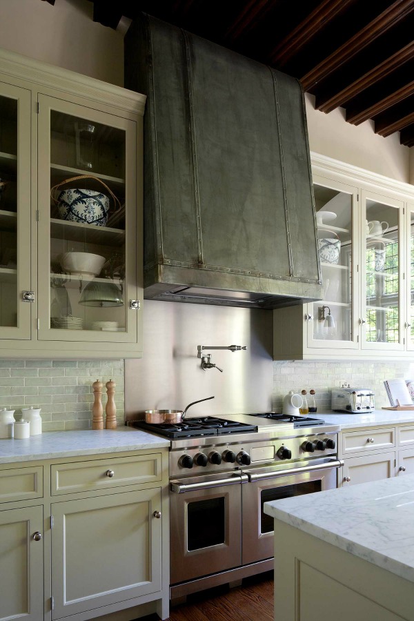 New England style kitchen cabinets flank a Wolf range. Chromed door catches, simple glazed wall cabinets, and extraction canopy clad in zinc. The canopy is antiqued with acid and wax. #kitchendesign #londonkitchen #bespokekitchen #artichoke