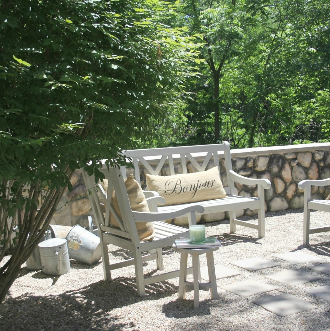 French country courtyard with bench, chairs, and Bonjour pillow. Hello Lovely Studio. #hellolovelystudio #frenchcourtyard #frenchcountry #peagravel #stone #garden