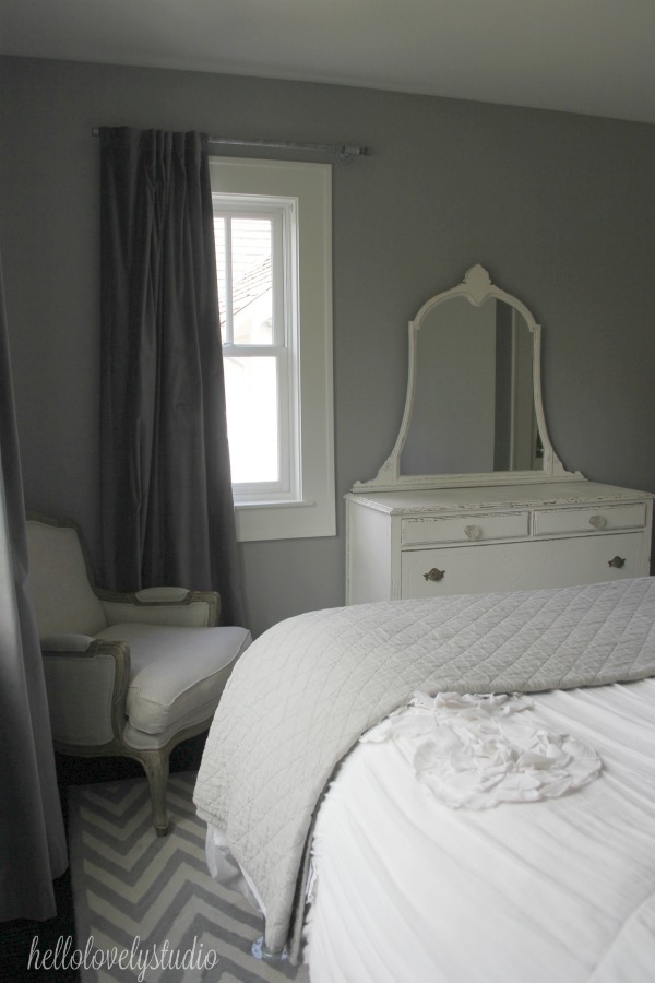 Farmhouse style bedroom with vintage whit dresser, European linen arm chair, and herringbone area rug. Paint color on walls is Benjamin Moore Stonington Gray. #hellolovelystudio #farmhousebedroom #shabbychic #benjaminmoorestoningtongray