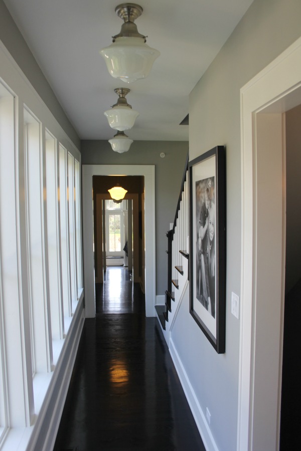 Reflective black flooring in a hallway with schoolhouse lights and medium grey paint colors. Come score the exact colors used on Hello Lovely. #interiordesign #greypaint #paintcolors #blackfloors #industrialfarmhouse