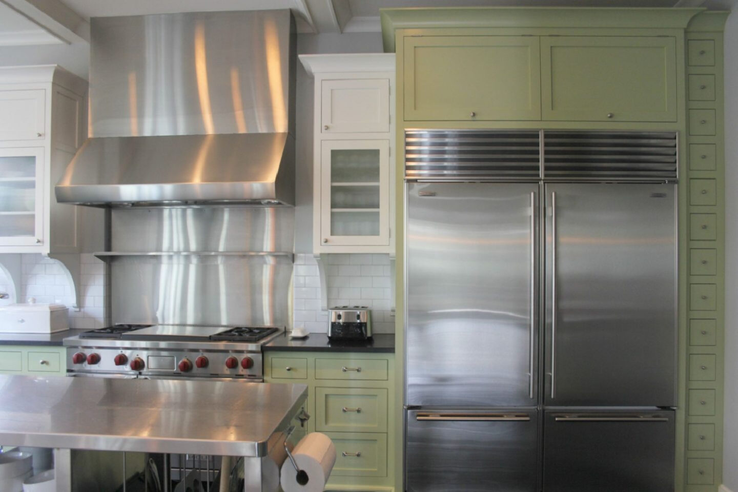 Green cabinets, a commercial stainless frig, and a restaurant style stainless work table in a modern farmhouse kitchen in a renovated 1875 Barrington farmhouse - Hello Lovely Studio.