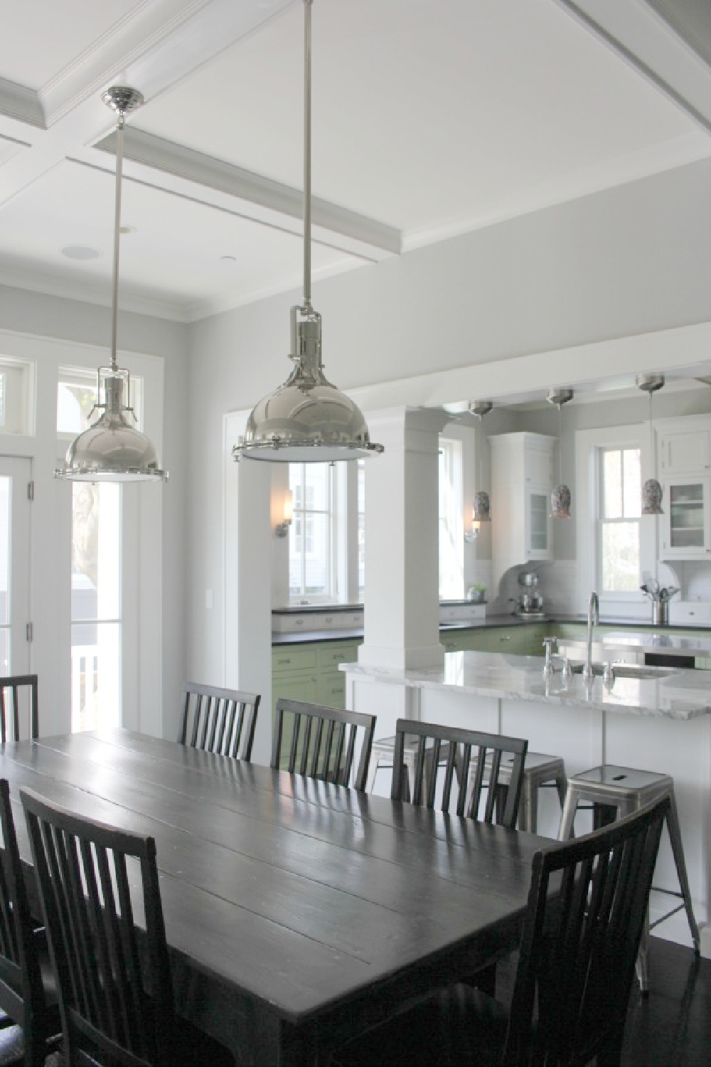 Polished nickel pendants over a farmhouse dining table with black chairs in a modern farmhouse kitchen - Hello Lovely Studio.