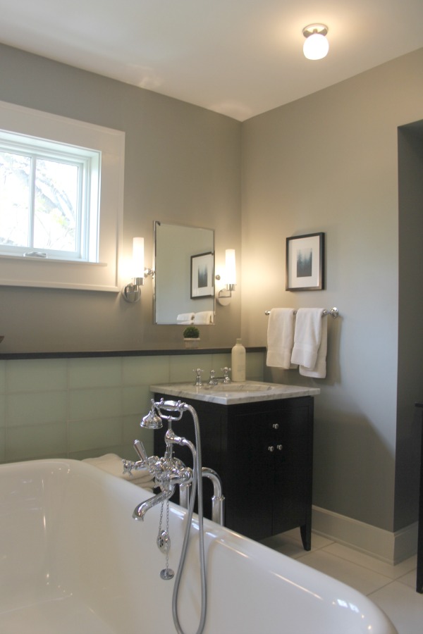 Traditional style bathroom with freestanding Waterworks tub, black vanity with carrara marble, and glass tile backsplash. #hellolovelystudio #bathroomdesign #freestandingtub #blackvanity #greywalls #benjaminmoorestoningtongray