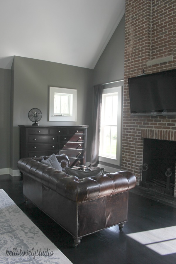 Benjamin Moore Peinture gris platine sur les murs d'une chambre de ferme moderne avec canapé Chesterfield en cuir et cheminée en brique rouge. #hellolovelystudio #bedroom #modernfarmhouse #benjaminmoore #platinumgray #greywalls