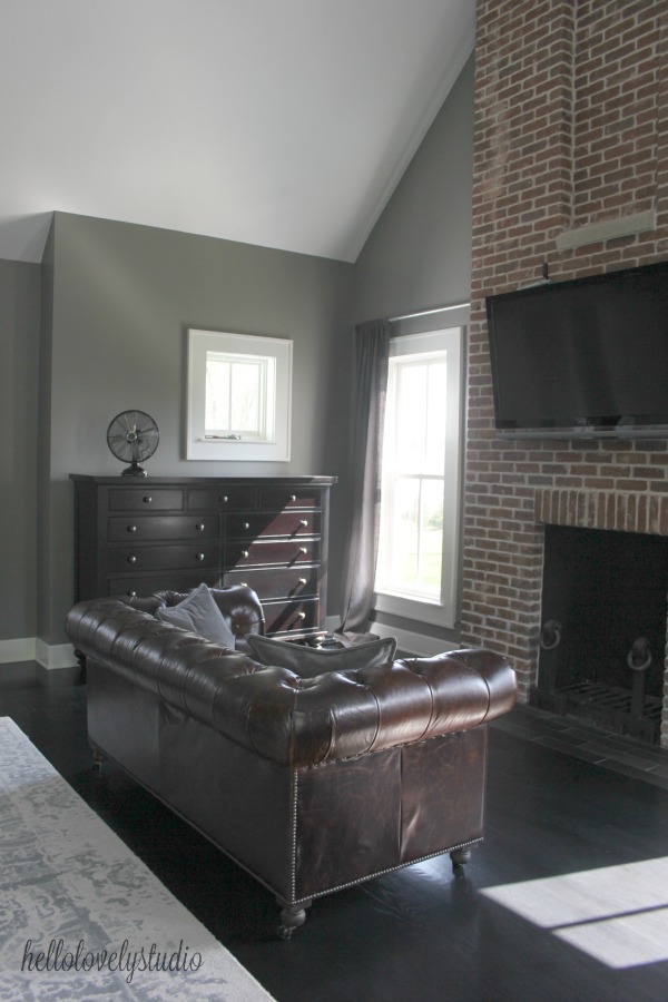 Benjamin Moore Platinum Gray paint on walls in a modern farmhouse bedroom with leather Chesterfield sofa and red brick fireplace. #hellolovelystudio #bedroom #modernfarmhouse #benjaminmoore #platinumgray #greywalls