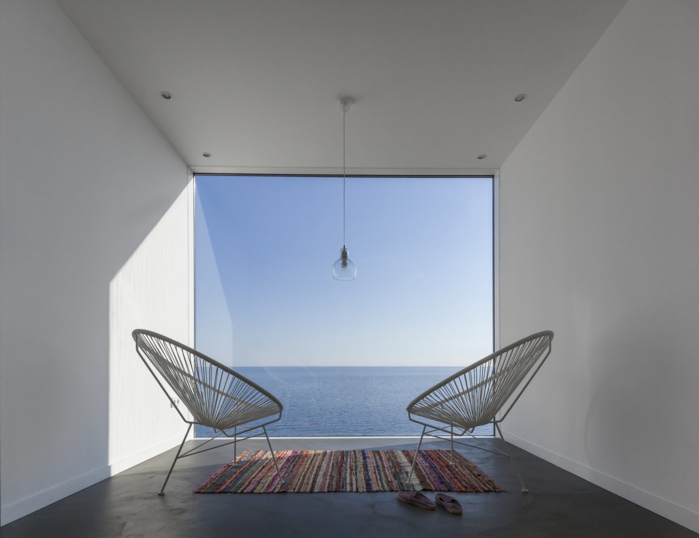 Two modern wire chairs in a small space overlooking the ocean. A wall of glass provides an unobstructed view. #beachhouse #oceanfront #modernarchitecture #wallofglass